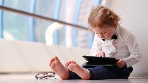Little cute barefoot girl sits on floor with tablet pc in gallery