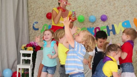 Six kids catch soap bubbles, which lets funny entertainer at children party. Inscription Happy Birthday on wall