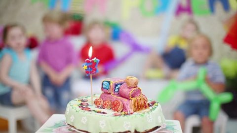 Birthday cake with candle is on table and kids expect treats at children party. Focus on cake