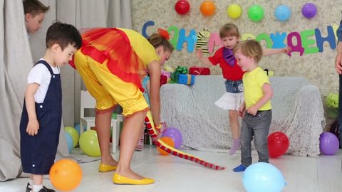 Four kids jump and play with funny entertainer at children party. Inscription Happy Birthday on wall