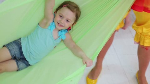 Little smiling girl lies in swaying hammock indoor at kids party