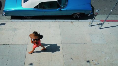 Anonymous woman in red dress walking by retro American car in Los Angeles, California. Overhead view. Slow motion. Stockvideó