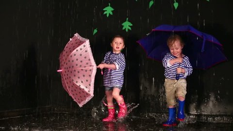Little girl with boy in striped vest under a blue and pink umbrellas stomp the puddle
