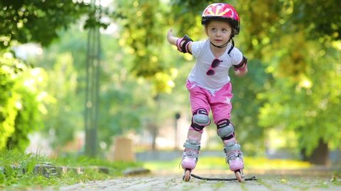 Little girl in protective equipment roller-skates on walkway at park