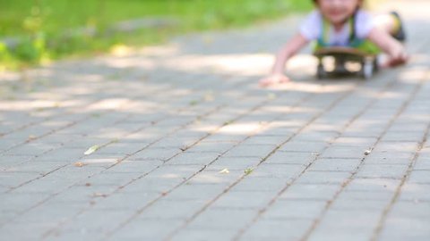 Little girl rides down park alley lying on skateboard