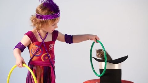 Little girl in costume magician training kitten with hoops