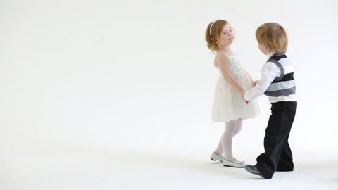 Little pretty smiling girl and boy dance in white studio