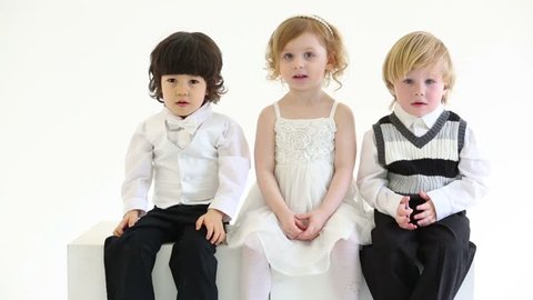 Little happy girl and two boys sit on white big cubes in white studio