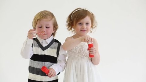 Little smiling girl and boy blow bubbles in white studio