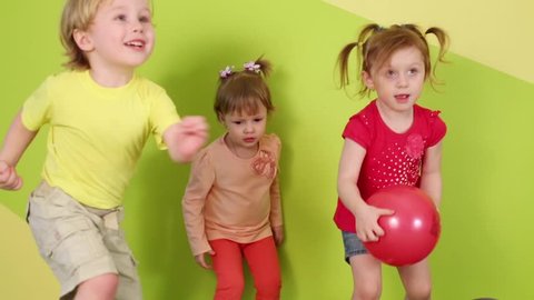 Two girls and boy jump and run among falling soap bubbles