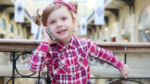 Little cute girl stands near wrought railings and talks to mobile phone at mall