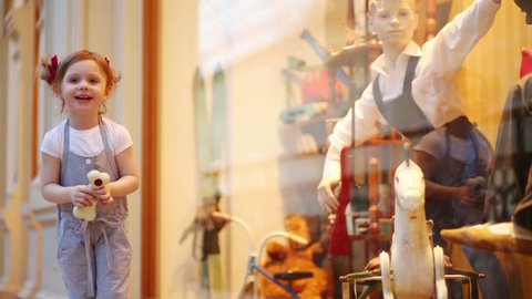 Little cute girl holds toy bone and looks at shop window in mall