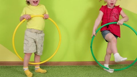 Little boy and pretty girl play with yellow and green hoops in bright room