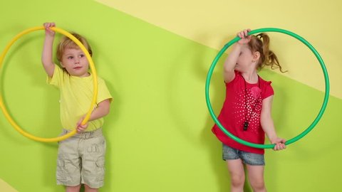 Little boy and girl play with yellow and green hoops in bright room