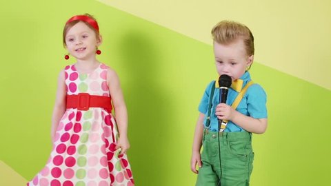 Little girl in adult shoes dances and boy in bright clothes sings into microphone