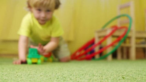 Little blonde boy plays with toy train on floor with carpet