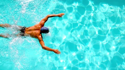 Athletic swimmer swimming across the pool overhead in slow motion