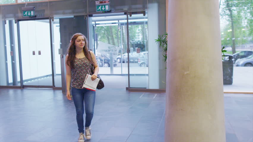 Cheerful student arrives for an interview at large modern college or university.