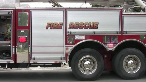 Video close up of a fire truck with the words Fire Rescue parked in front of a house fire.