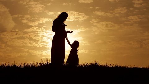 Silhouettes young mother and  her 3 year old daughter at sunset