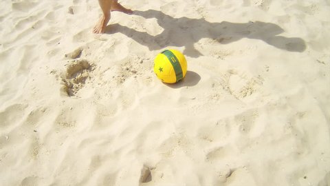 Man dribbles a soccer ball past defenders on sand.