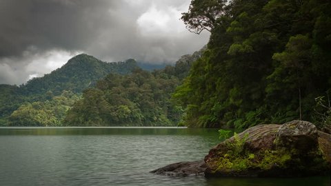 Timelapse white clouds and grey clouds moving fast over tropical lake, mountains and forest in the Philippines