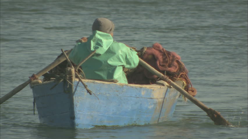 A man rowing his traditional small fishing boat, with a pan down to the oar, Morocco, 2013