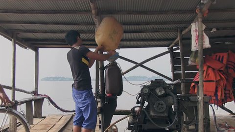  Cambodia -  november 2013.  Boat driver filling engine oil using funnel and plastic oil can