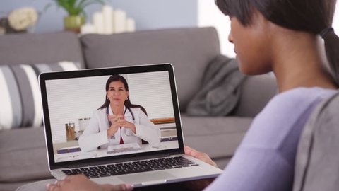 African woman video chatting with doctor. Tele medicine check up from home on laptop over the internet