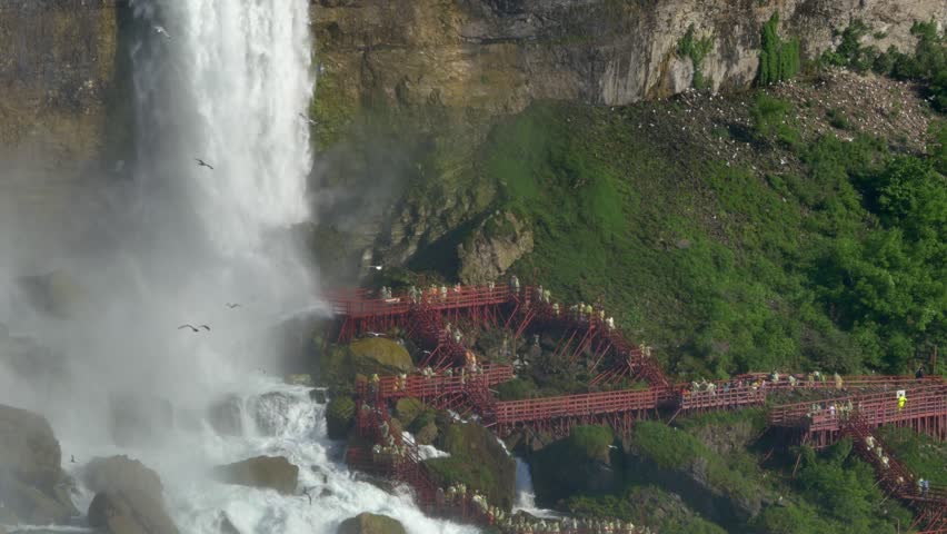 Tourists in yellow raincoats walk on the staircase at the Cave of the Winds attraction. 