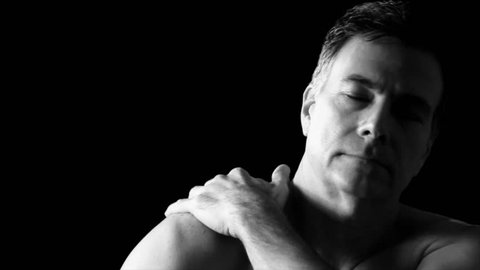 A man rubbing his shoulder and neck as if suffering from muscle or joint pain.