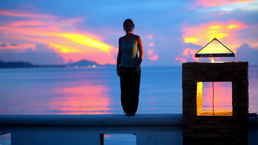 Young woman doing yoga exercise over the sunset background and standing near shines lantern. 1920x1080