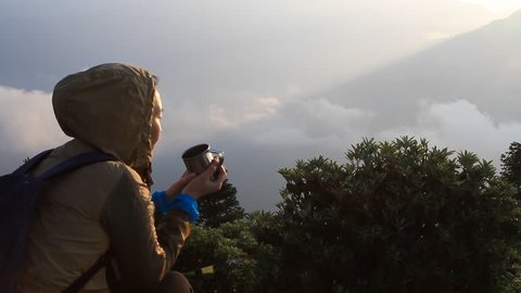 Asian woman watching the sunrise from the observatory of Poon Hill and drinking a cup of coffee in Nepal