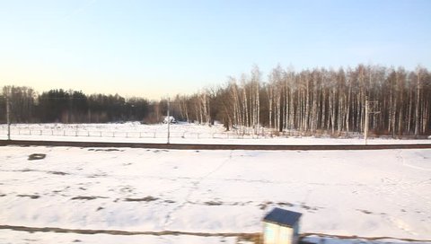Side view from a passenger train of the countryside of Russia at winter with sun glowing above the trees (hd, 1920x1080, high definition, 1080p)