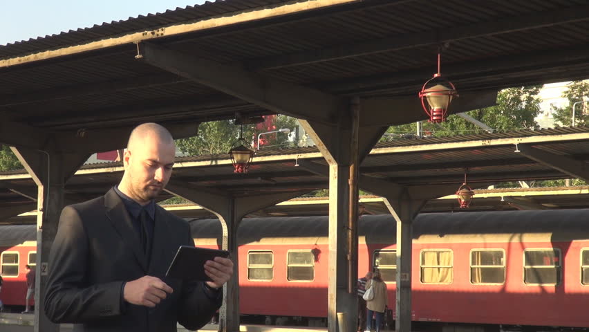 PAN view commuter walking on rail platform working on tablet sunny day outside