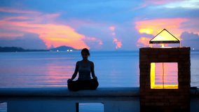 Young woman doing yoga and meditates over the sunset background. Video