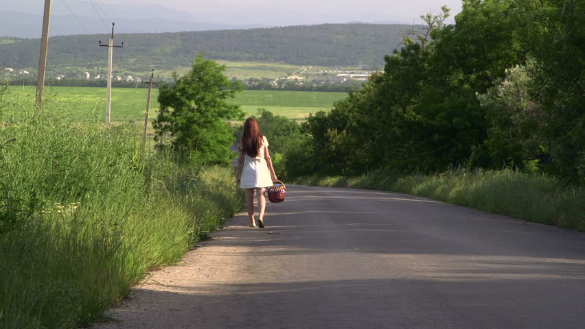 Young girl with basket walking along a country road rear view