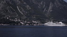 Cruise ship enters a port on a background of mountains.