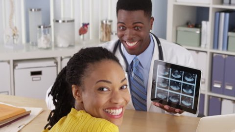 Black OBGYN using tablet to show ultrasound to patient at desk