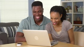 Happy young black couple laughing and watching funny video on laptop