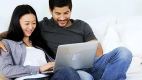Attractive young heterosexual ethnic couple relaxing modern home couch enjoying social media using wireless laptop technology close up
