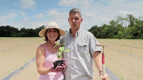 Couple standing in front of newly plowed field holding a hazelnut tree they will plant.
