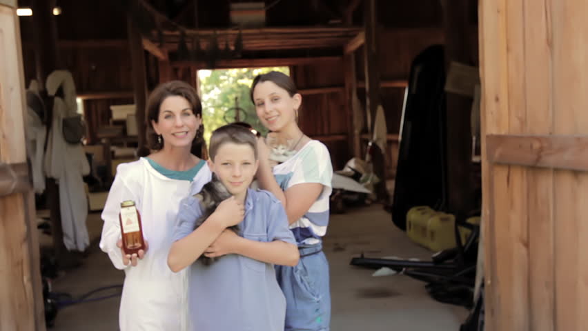 Portrait of Mother with kids in front of Barn. Mother is wearing a bee keeper uniform and holding Jar of Honey