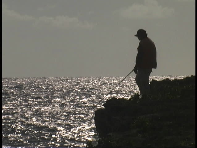 fisherman standing on cliff with ocean waters below