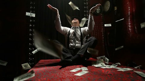 Italian gangster sitting on a table scatters packs of dollars. Rain of banknotes.