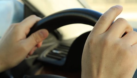 Man's hands holding steering wheel of car and tapping fingers 