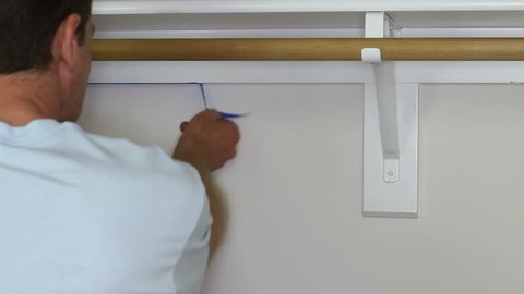 Man Removing Painter’s Tape. Adult male enters a small closet and removes blue painters tape from wall edges of shelves after he painted white on the walls in a home improvement project.
