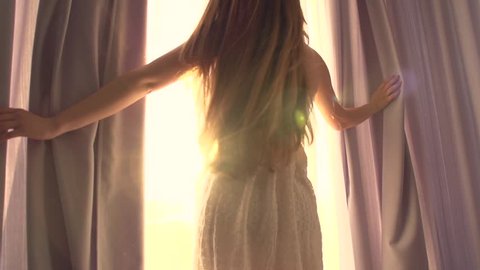 Beauty Girl opens curtains on big window and let the light in the room. Looking out the window. Slow motion video footage full hd 1920x1080. High speed camera shot 240 fps