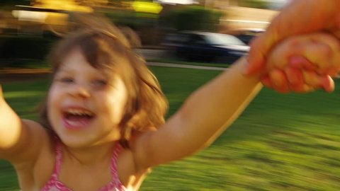 POV video of father spinning happy girl daughter child around in park at sunset. Slow motion.