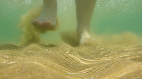 Underwater footsteps of a man in the shallow sea water on the sandy seabed. He is walking through the camera and passing over it. Half speed slow motion from 59p to 29p.